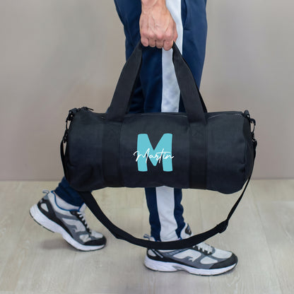 Personalisierte schwarze Sporttasche mit türkiser Initiale M und Name Martin, getragen von einem Mann als Trainingstasche