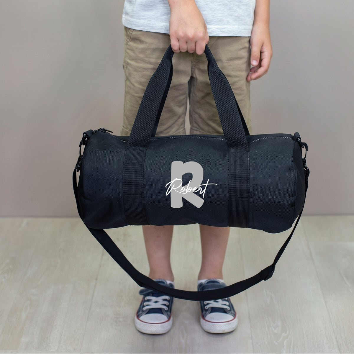 Schwarze Sporttasche für Kinder mit grauer Initiale R und Name Robert, getragen mit Schultergurt