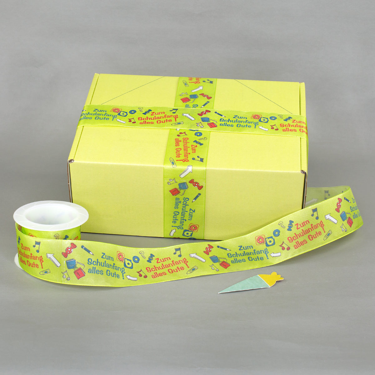 Geschenkband zur Einschulung als Dekoration an gelber Geschenkbox mit zusätzlichem Band auf Rolle