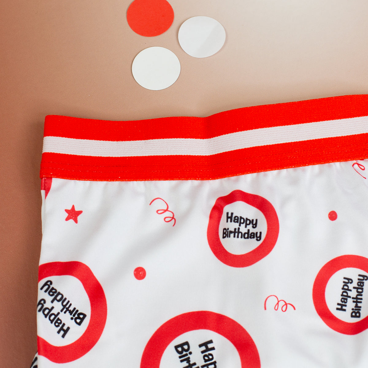 Detailaufnahme vom roten Bund der Boxer Shorts mit weißem Streifen und Happy Birthday Aufdruck auf weißem Stoff