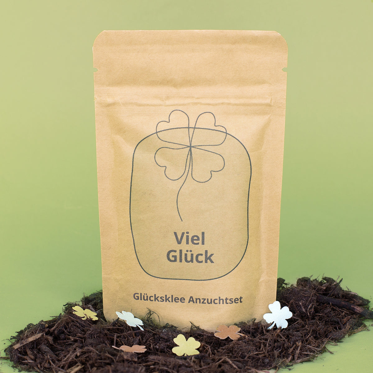Viel Glück Anzuchtset in brauner Kraftpapiertüte mit Kleeblatt-Motiv zwischen Erde und Streudeko
