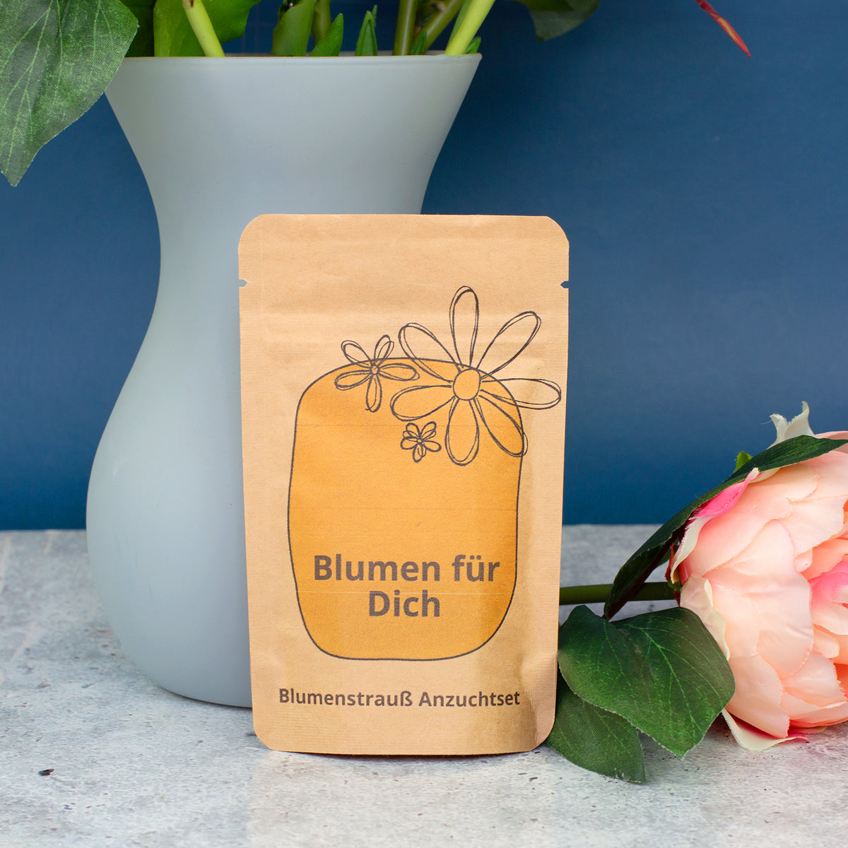 Blumen für Dich Anzuchtset in brauner Tüte vor blauer Vase und rosa Blüte, dekoratives Geschenkset zum Selberziehen von Blumen