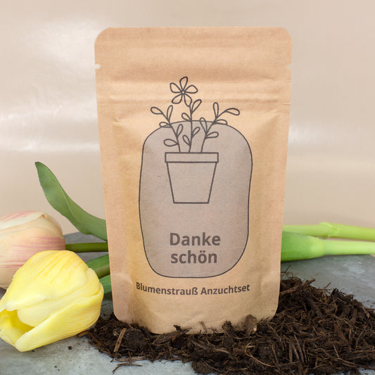 Danke schön Anzuchtset in brauner Kraftpapiertüte mit Blumenmotiv zwischen Erde und gelben Tulpen